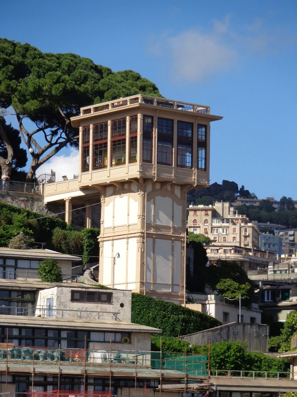 La stazione superiore in stile liberty dell'ascensore di Castelletto Levante, una torre color crema con grandi vetrate, tra pini marittimi e palazzi sulla collina