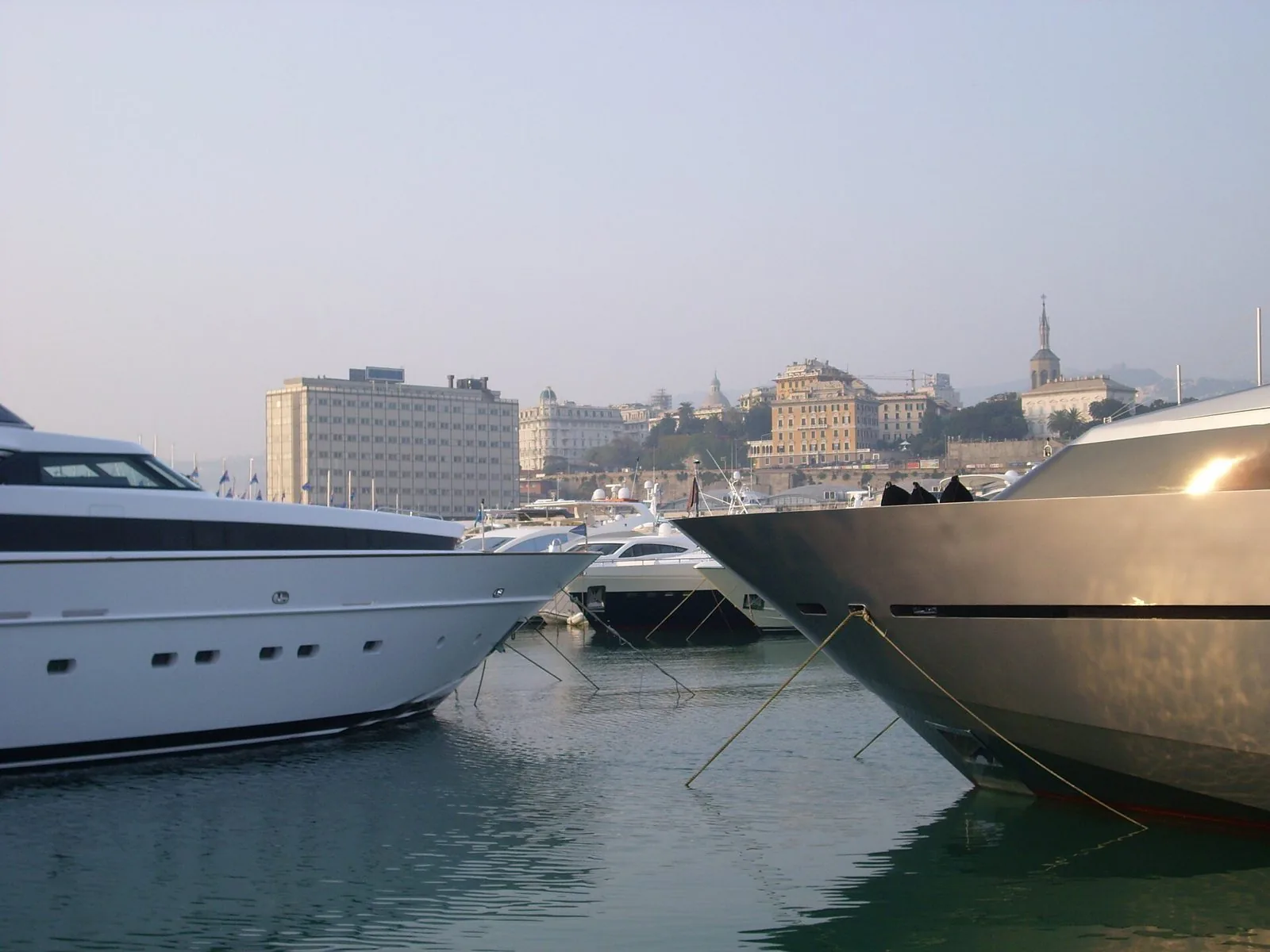 Yacht ormeggiati in banchina durante il Salone Nautico, con i palazzi di Genova sullo sfondo