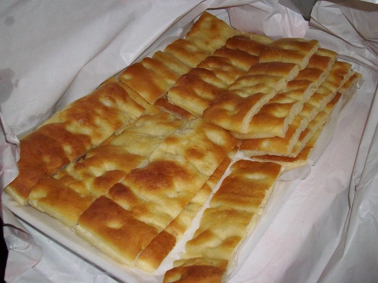 Tranci di focaccia genovese dorata appena sfornata, adagiati su carta da forno