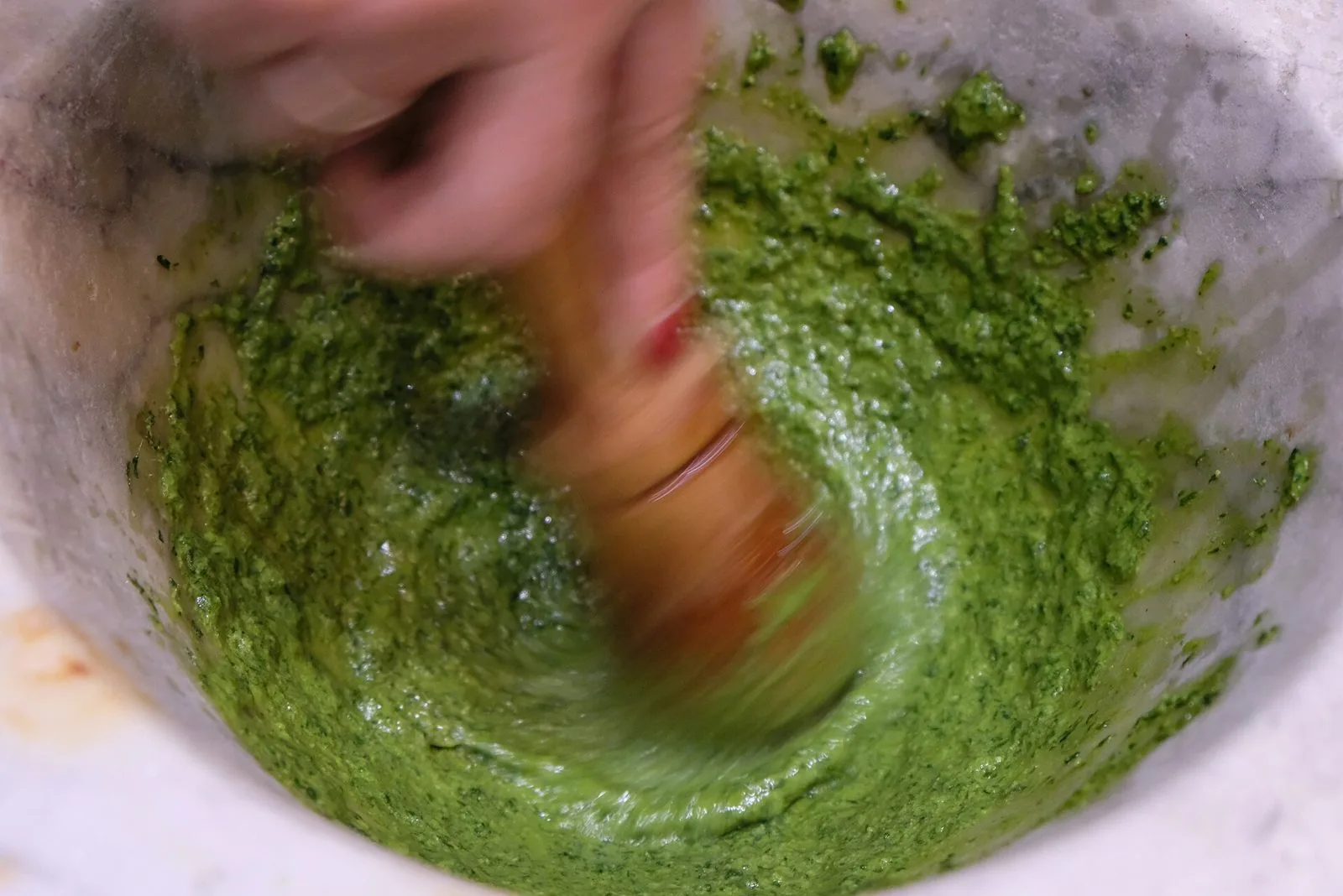 Pesto genovese preparato a mano in un mortaio di marmo con pestello di legno