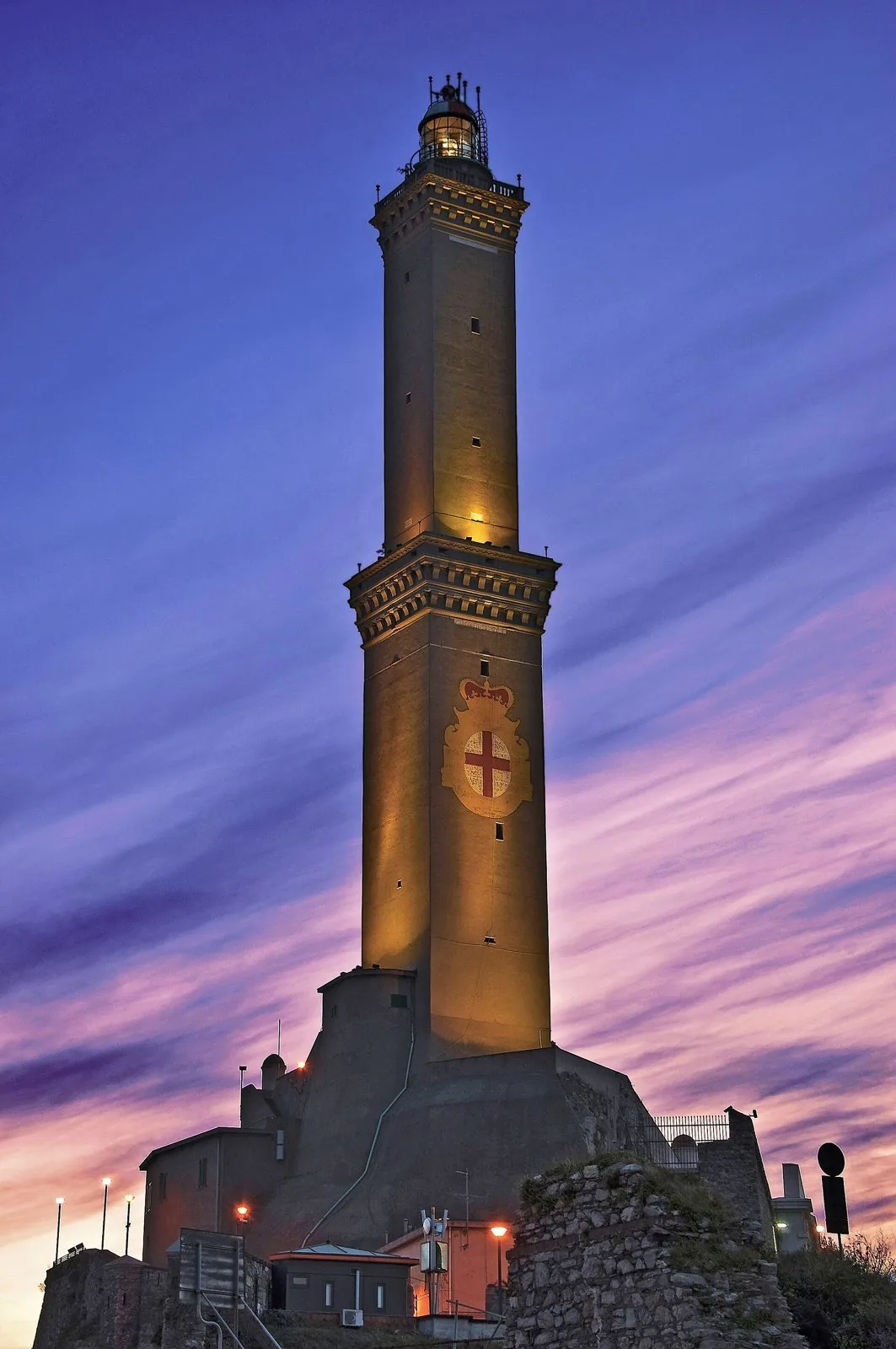 La torre della Lanterna di Genova illuminata al tramonto, con lo stemma della città sulla facciata